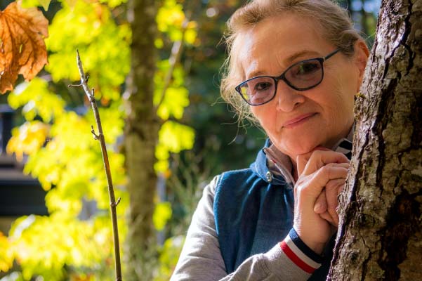 Woman with glasses leaning against a tree in the sunlit woods of Northern Michigan.