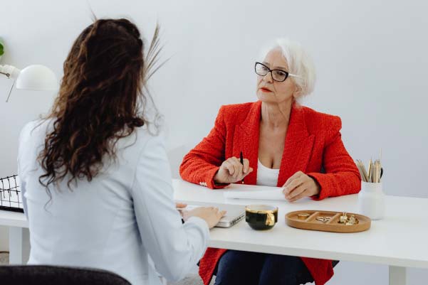 A dark-haired woman in white assisting an older woman in red with land financing for her dream home in Northern Michigan.