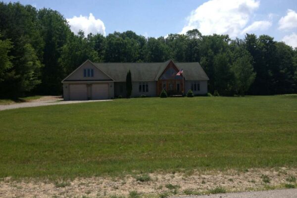 View across the lawn of a long house with a two-car garage and tall entryway with large windows.