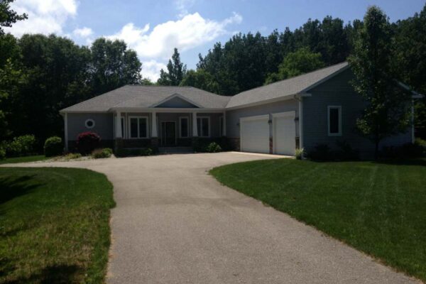 Driveway leading to a gray ranch home with a 3-car garage and covered porch.
