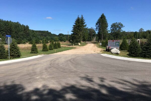The entrance to Big Sky residential property development community with a large For Sale sign, decorative rocks, and young pine trees.