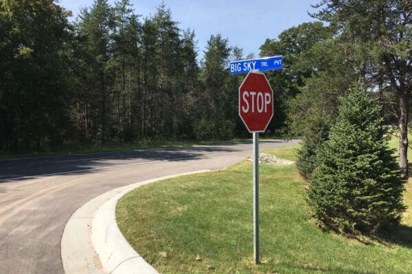 Stop sign at the end of Big Sky Trail with pine trees on both sides of the paved blacktop road.