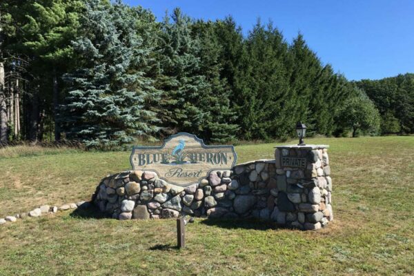 Blue Heron Resort property development sign built of large fieldstones with large blue spruce trees in the background.