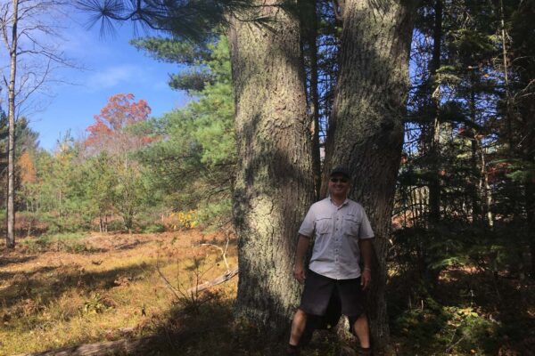 Smiling man leaning against a very large hardwood tree near the Carpenter Creek property.
