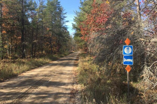 Dirt road through the woods with signs marking that food and hotels are up ahead.