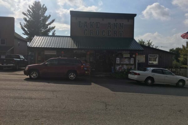 Front facade of the Lake Ann Grocery building during business hours with cars parked out front.