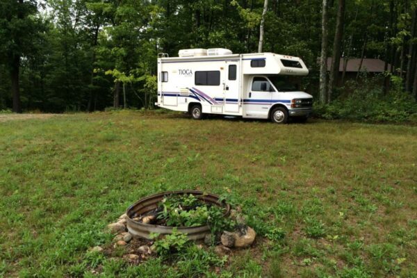 White Tioga RV parked near the tree line with a fire pit in the foreground.