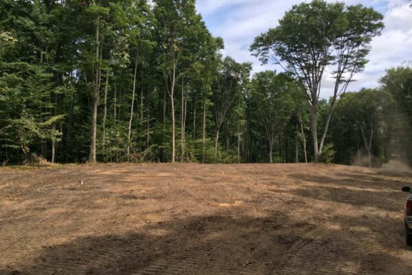 The edge of a freshly cleared and graded 10-acre lot bordered by mature hardwood trees.