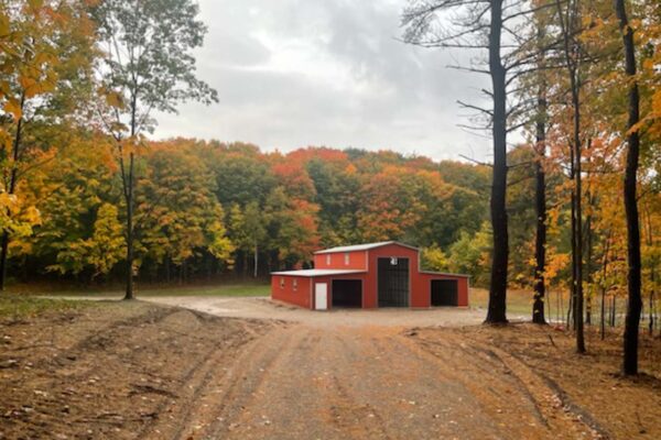 Image of a large red barn or polebarn being built in a clearing surrounded by the fall colors of Northern Michigan.