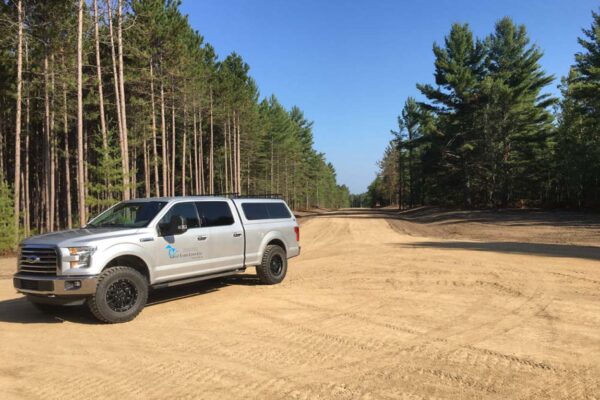 Great Lakes Land Co. company truck parked at the end of a dirt cul de sac lined with tall pine trees.