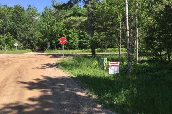 Stop sign at a four-way intersection in a dirt road lined with trees.
