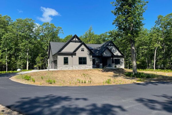 Stately gray two-story home with a circular driveway surrounded by mature hardwoods in the Woodland Trails property development in Grand Traverse County.